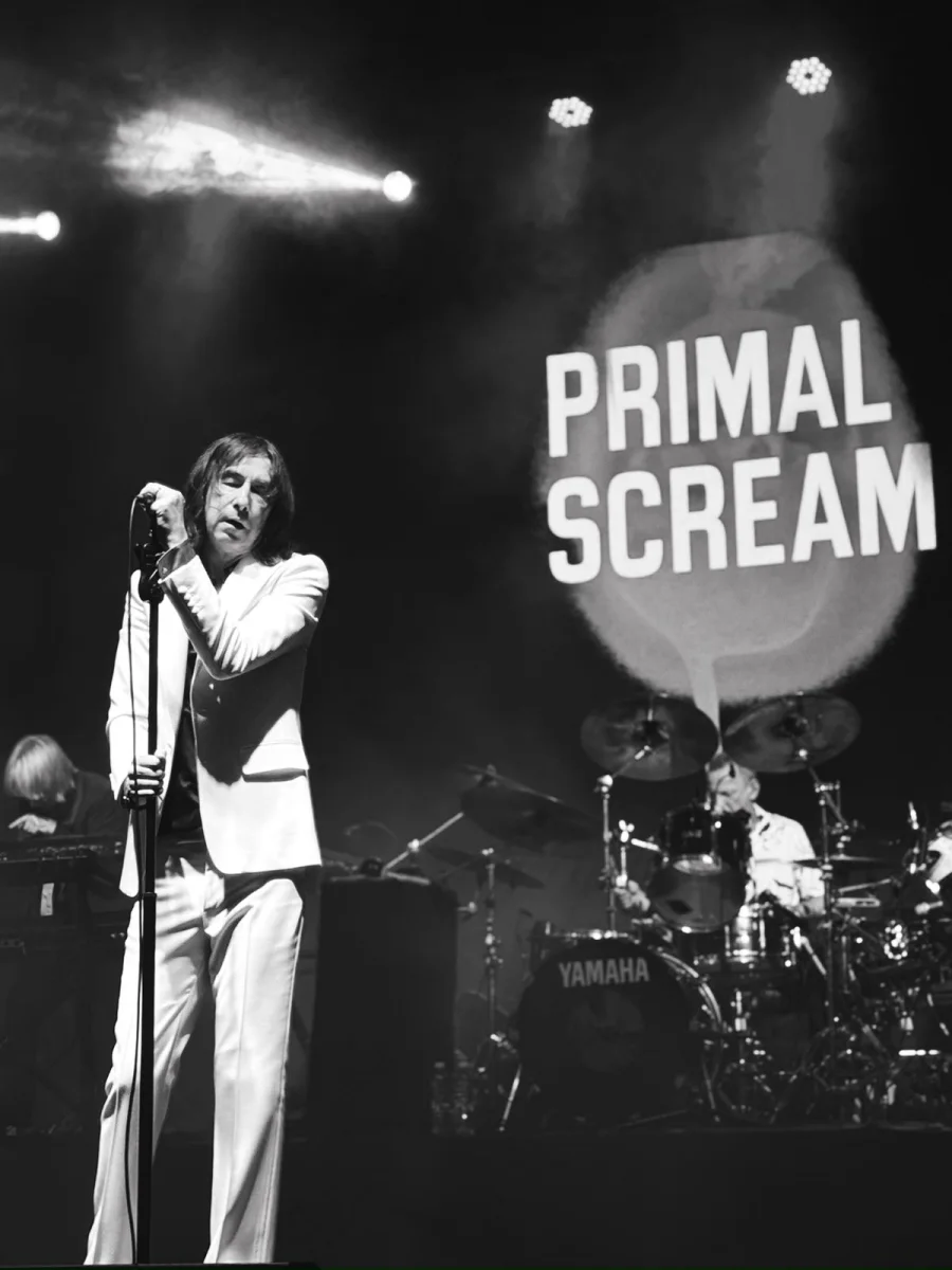 Bobby Gillespie cantando con Primal Scream, con el logo de la banda de fondo, foto de Maru di Rago